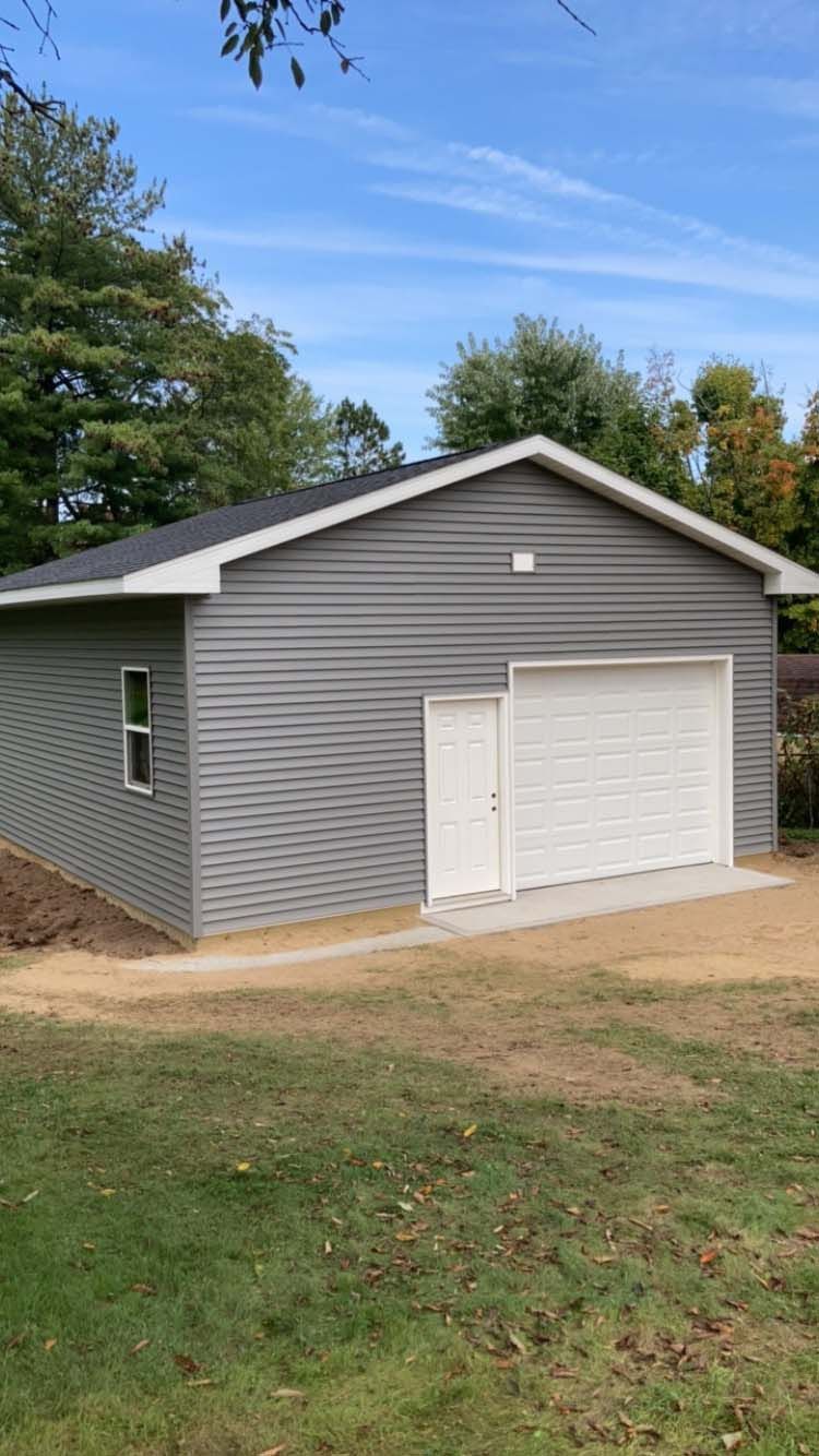 Gray garage with white door and overhead door on a lawn under a blue sky.