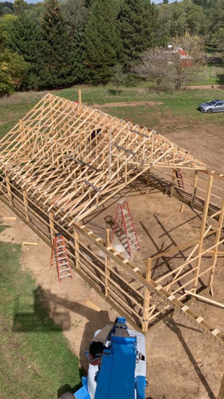 Construction of a wooden barn. Workers on the roof, scaffolding, and lift. Outdoors, daylight.