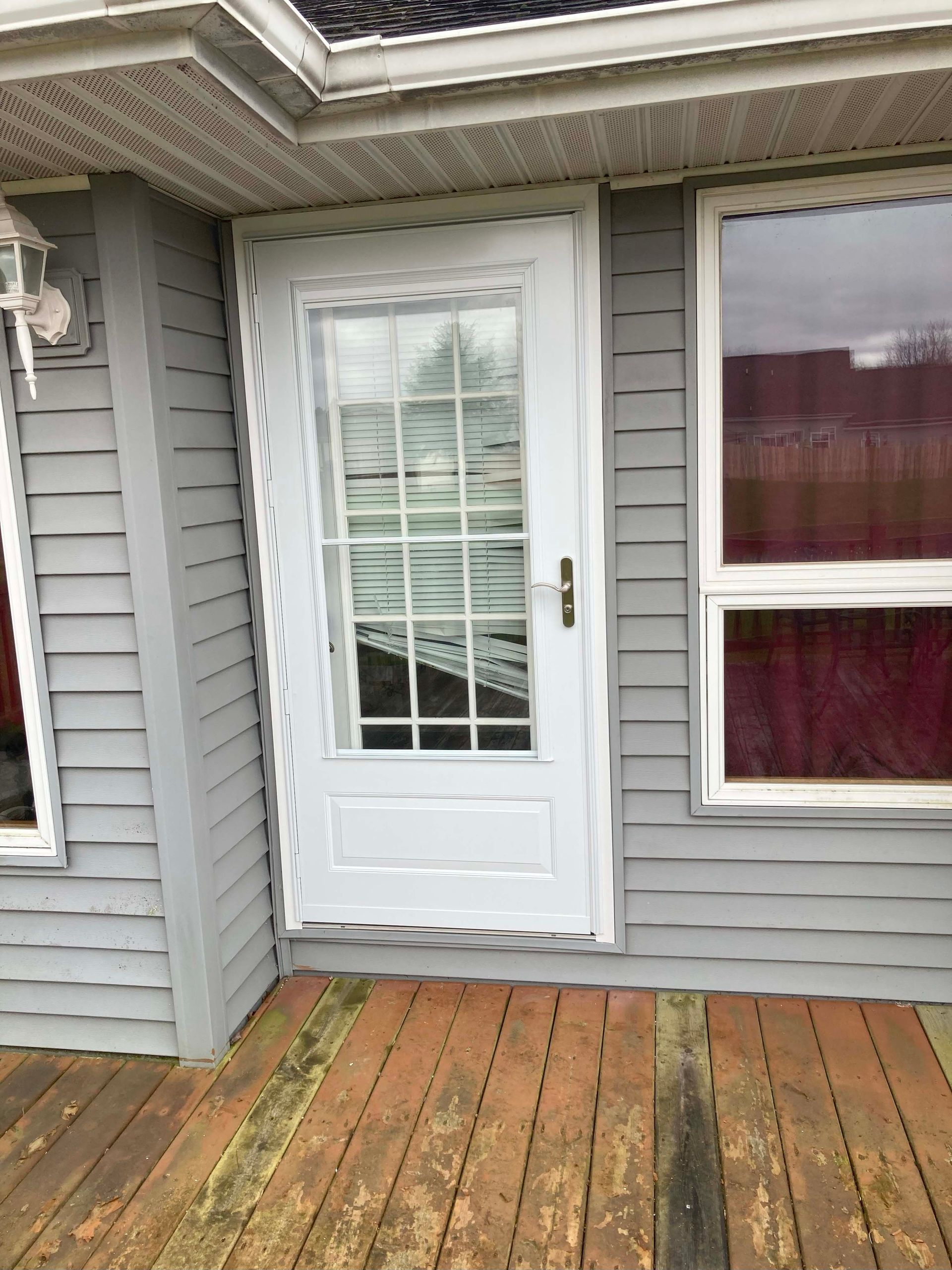 White screened door on a gray house with wood deck.