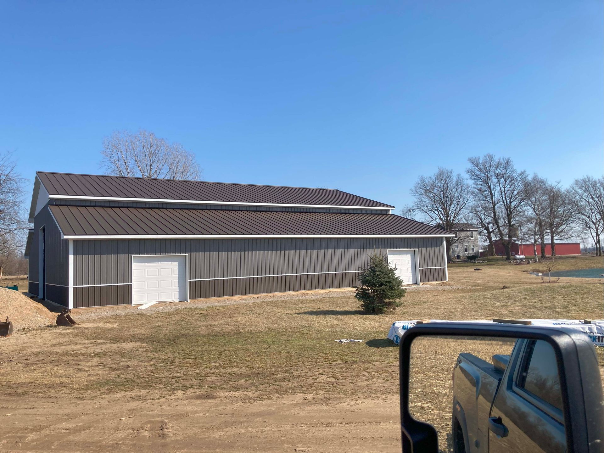 Gray metal barn under a bright blue sky. A truck is parked in the foreground.