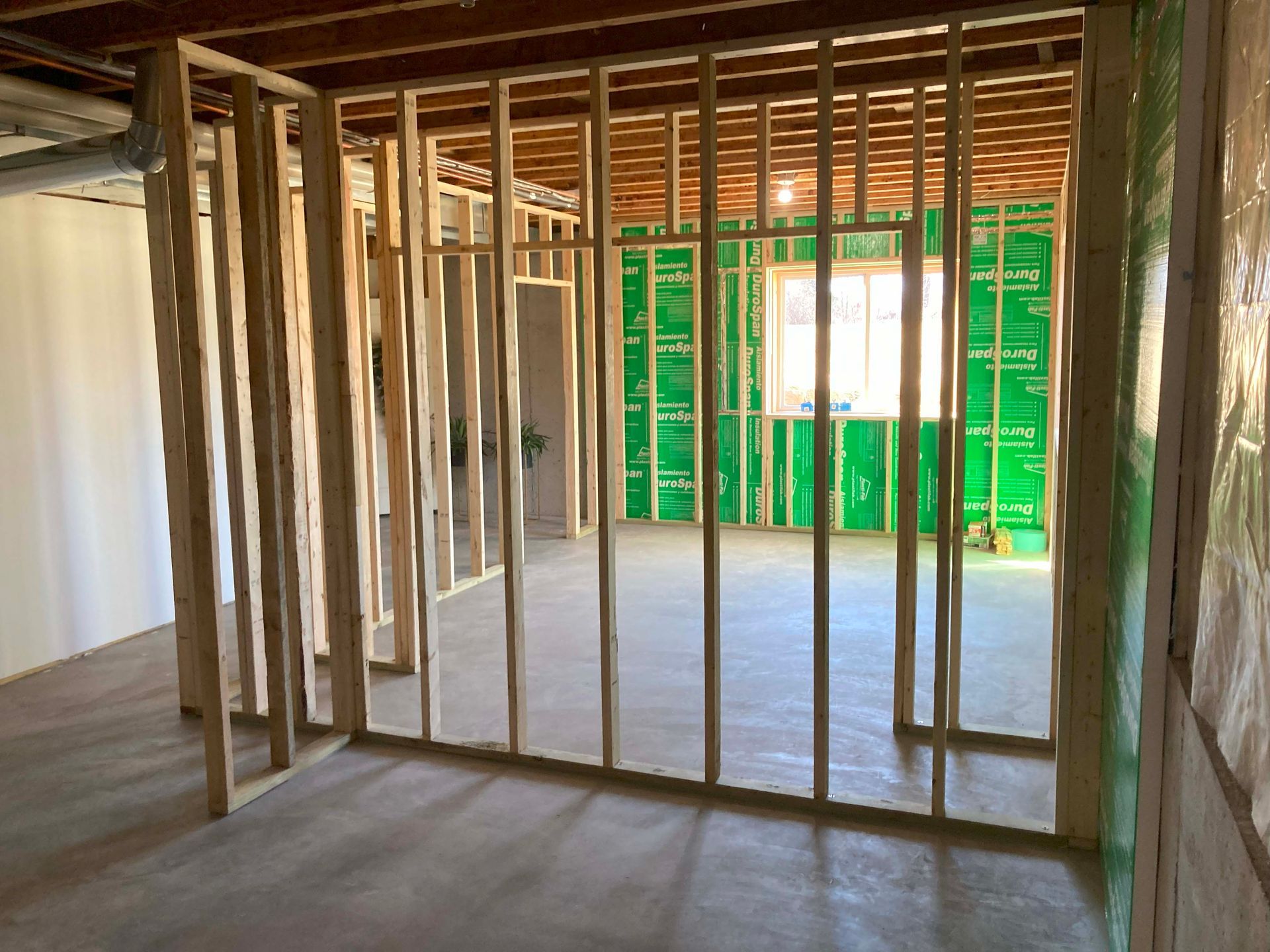 Interior view of a basement under construction with wooden wall framing. Green insulation is visible.