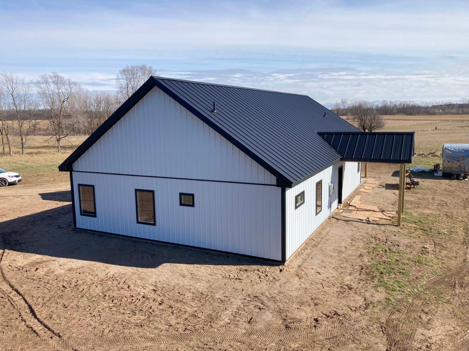 White and black farmhouse under construction in a field, with a dark roof.