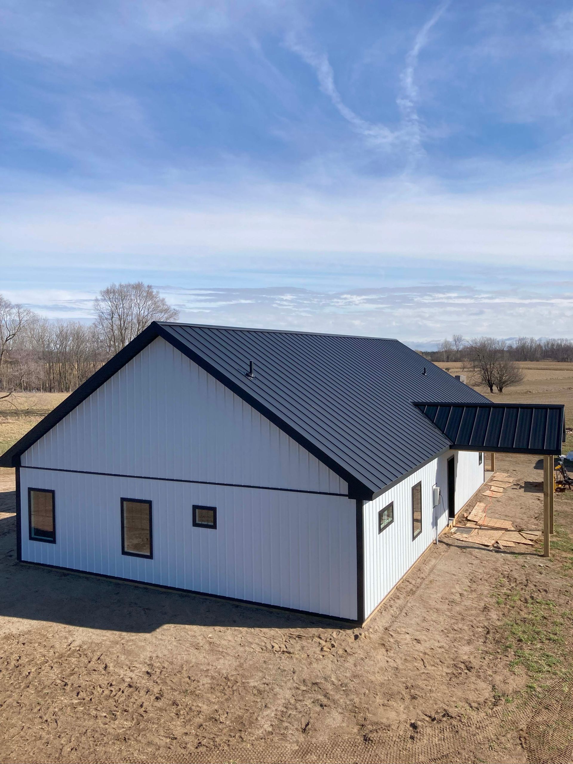 White house with black roof and trim on a field under a blue sky.