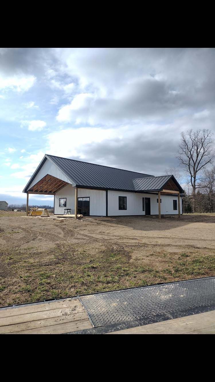 White building with dark roof under cloudy sky; brown dry field in foreground.