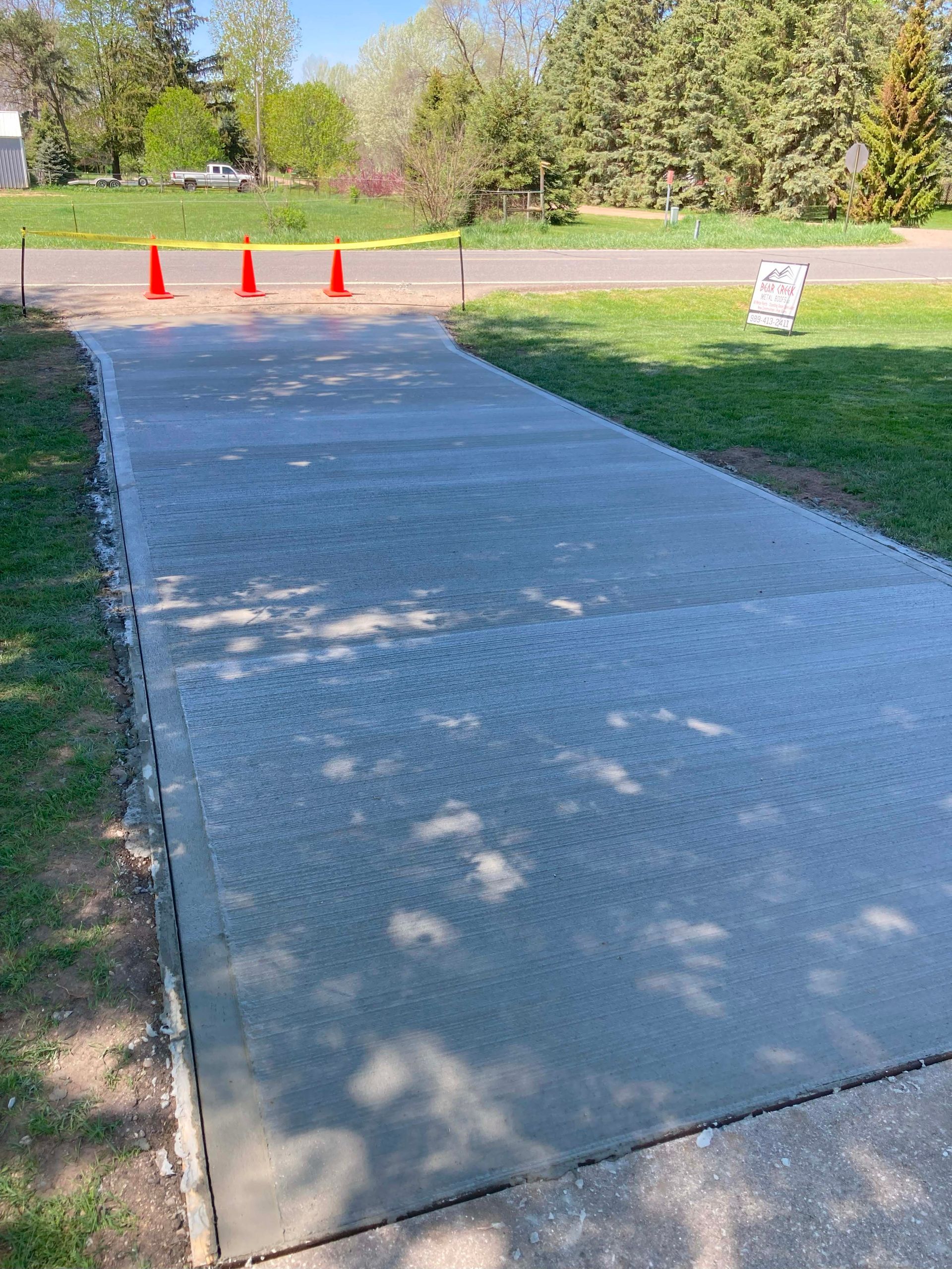 Newly poured concrete driveway with orange cones and grass on either side.