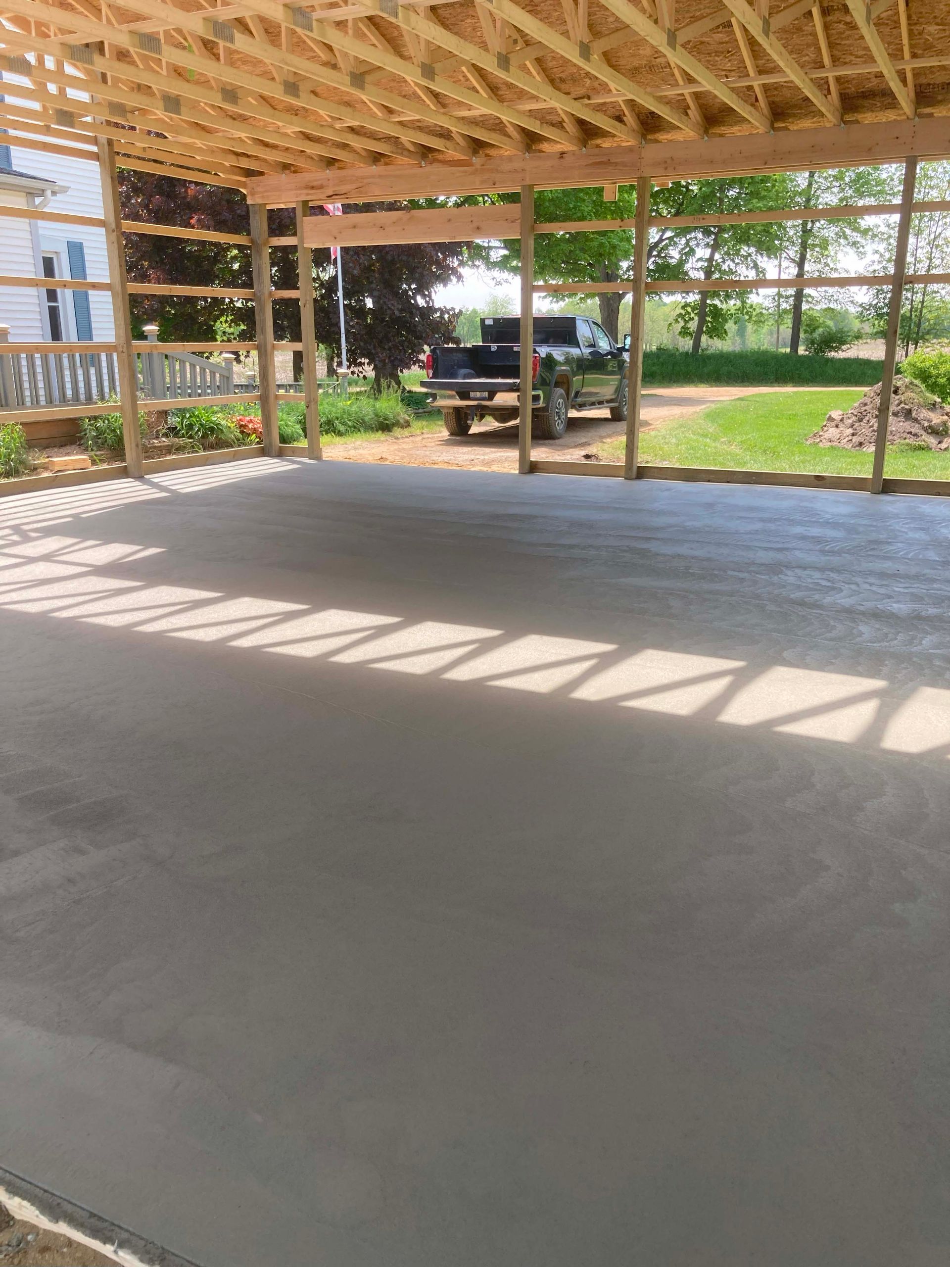 Newly poured concrete floor under a wooden frame structure, truck visible in the background.