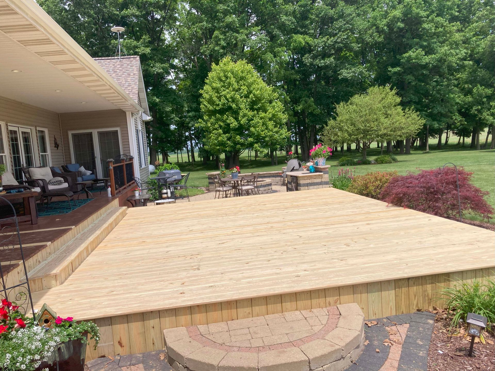 Large wooden deck extending from a house, with outdoor furniture and surrounding greenery.