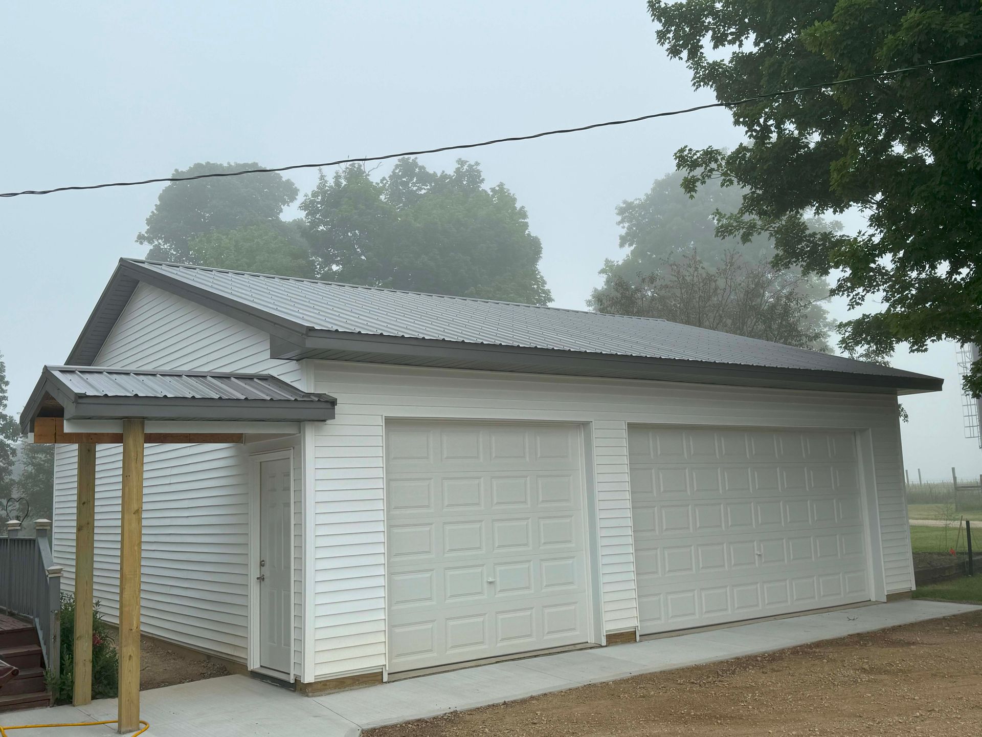 White two-car garage with attached entry under a small roof; foggy sky.