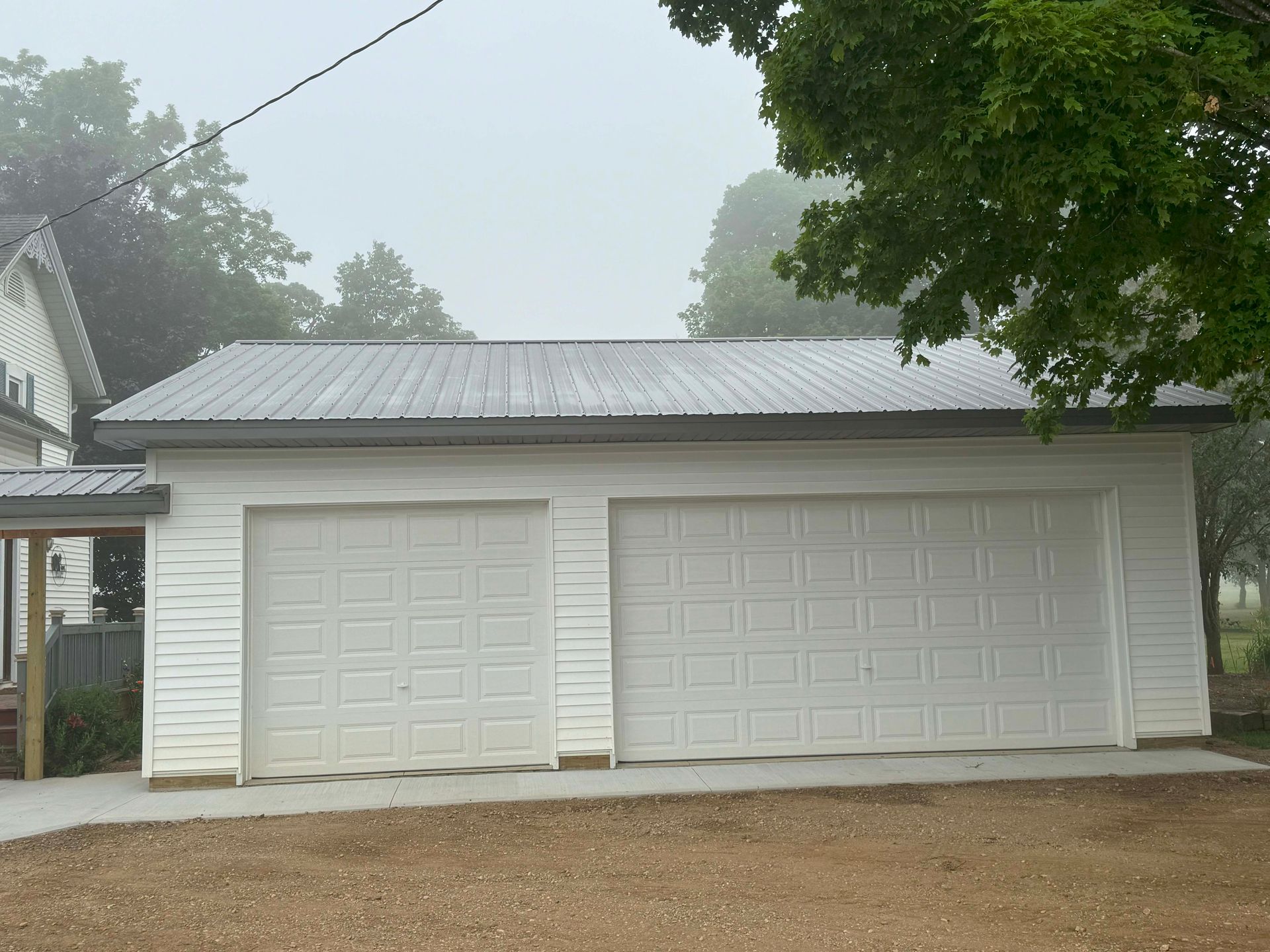 White two-car garage with metal roof, set against a foggy, overcast sky.