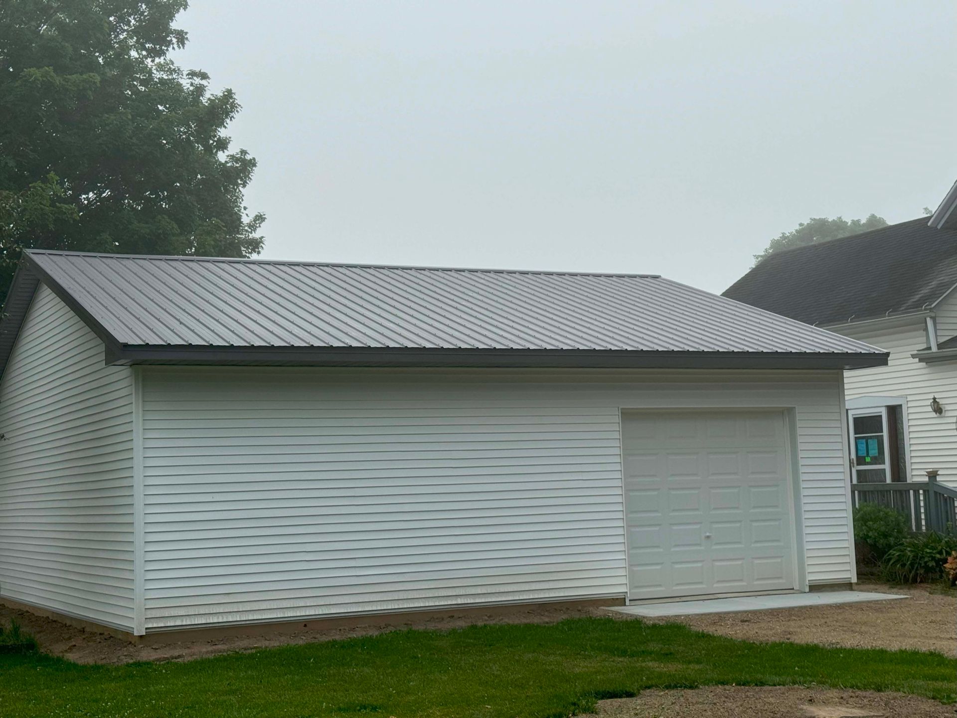 White garage with gray metal roof on a foggy day.