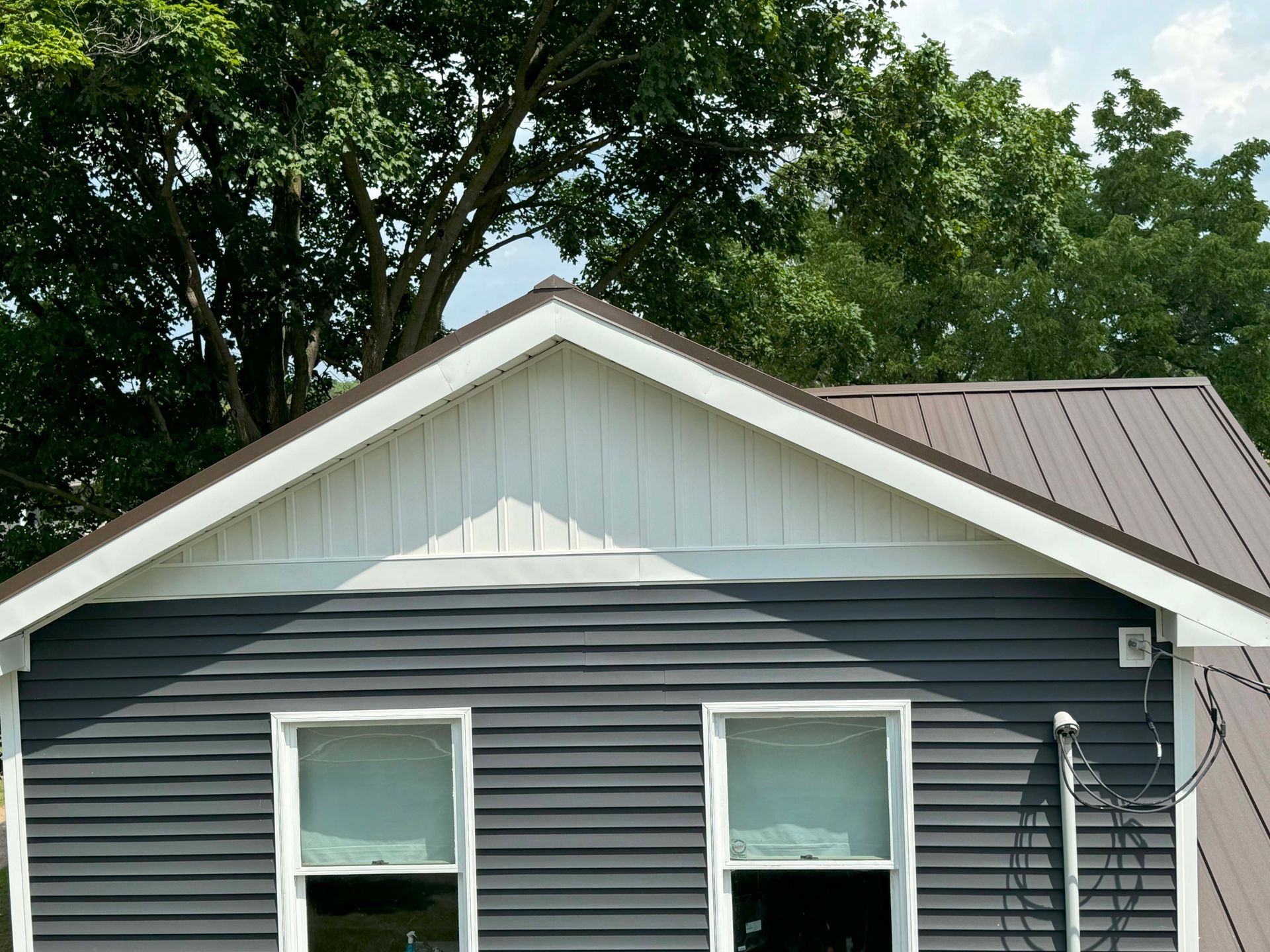 Gray house with a brown metal roof and white trim under a green tree.