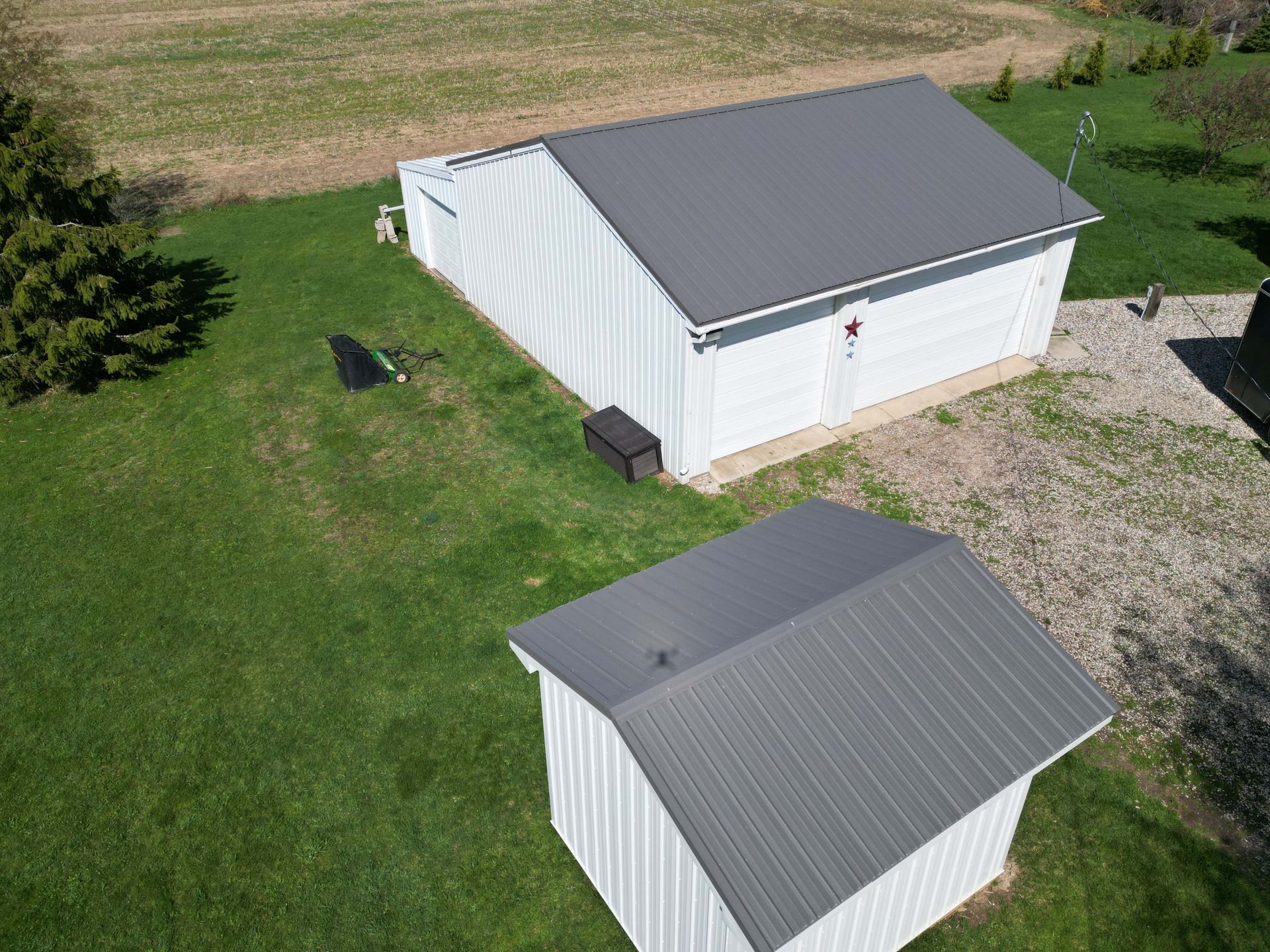 Two white sheds with gray metal roofs on a grassy lawn.