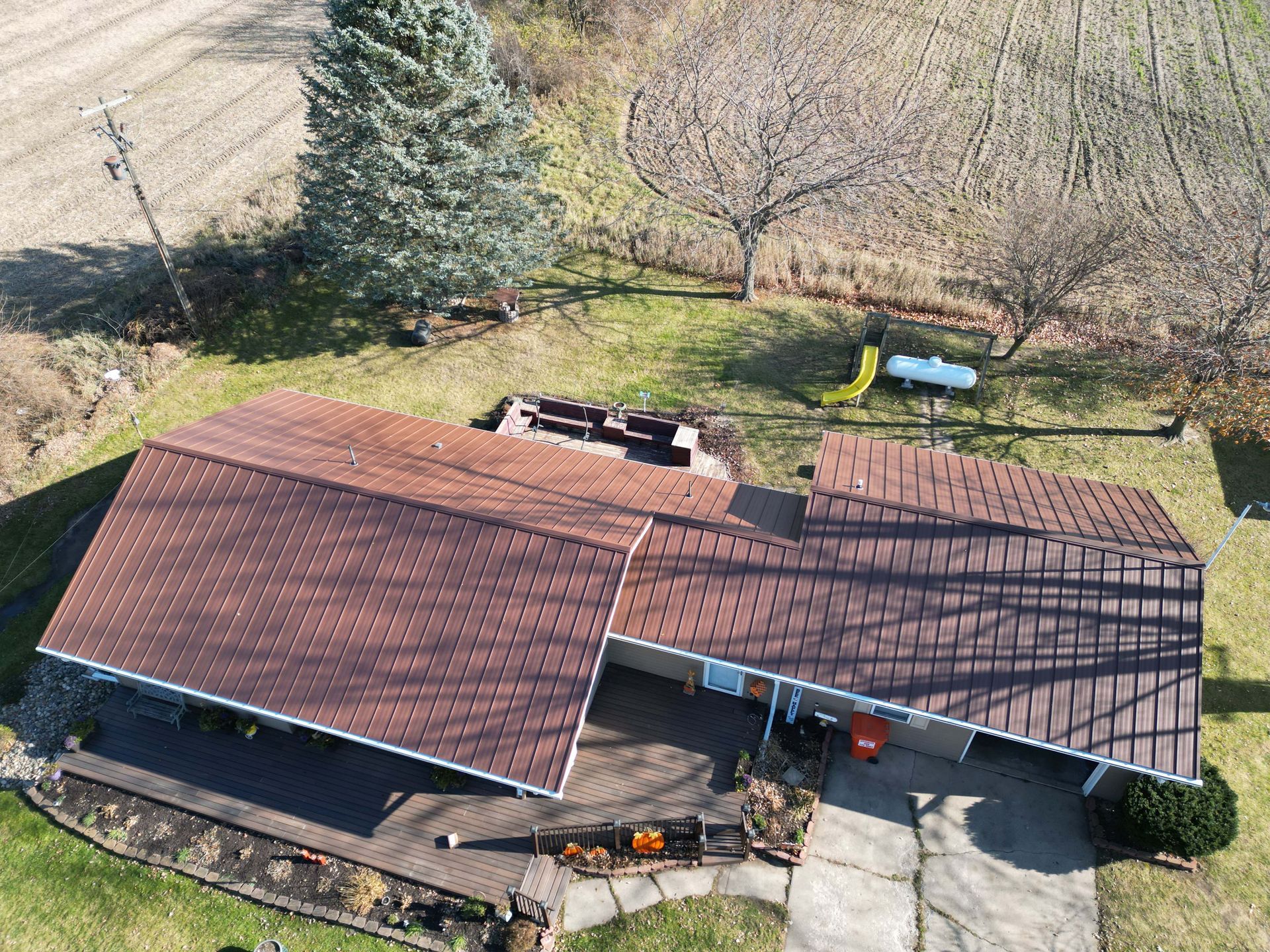 Aerial view of a brown-roofed house with a yard, fields, and a playground.