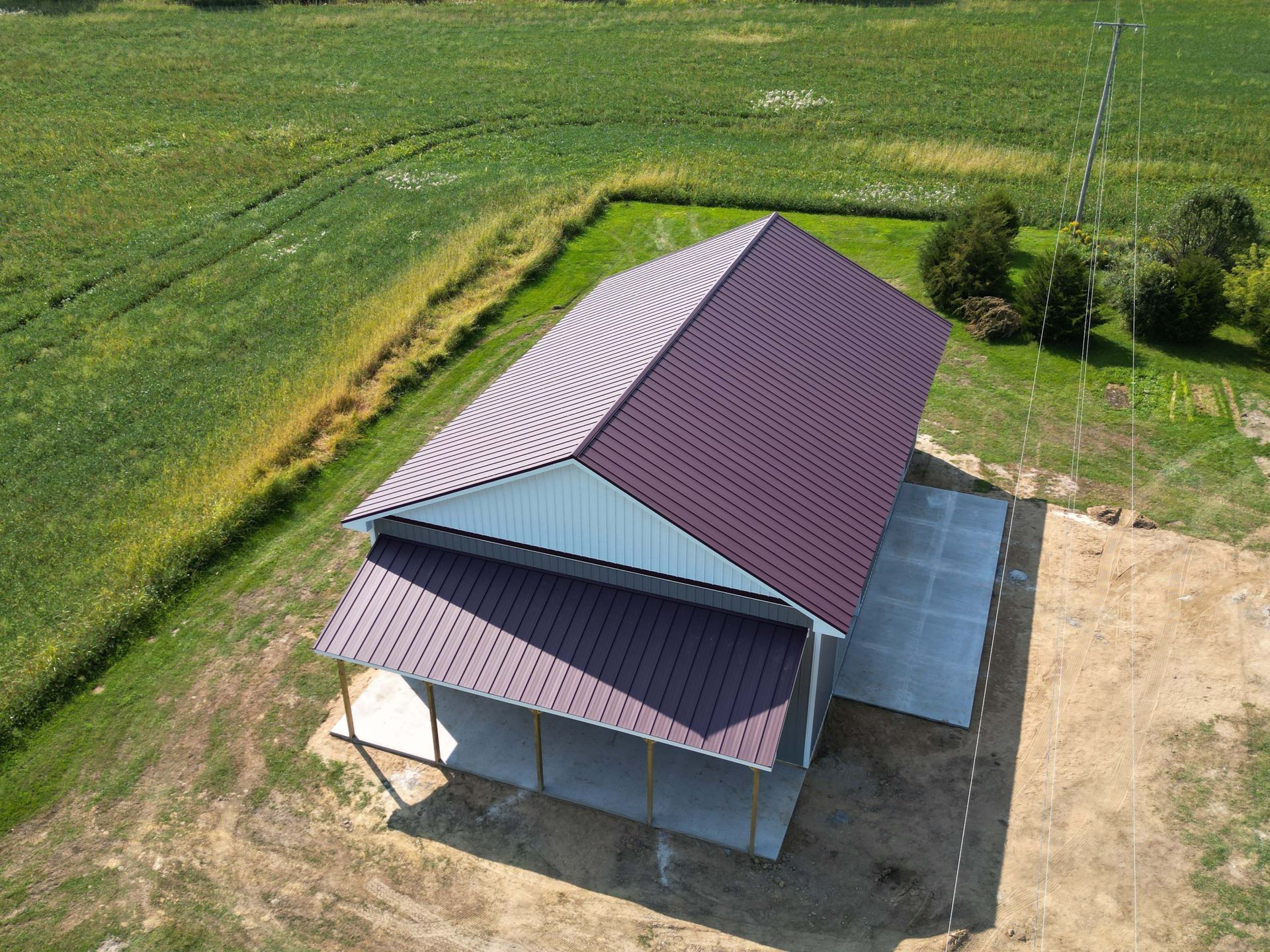 Aerial view of a metal-roofed barn with a concrete slab foundation on a green and brown rural landscape.