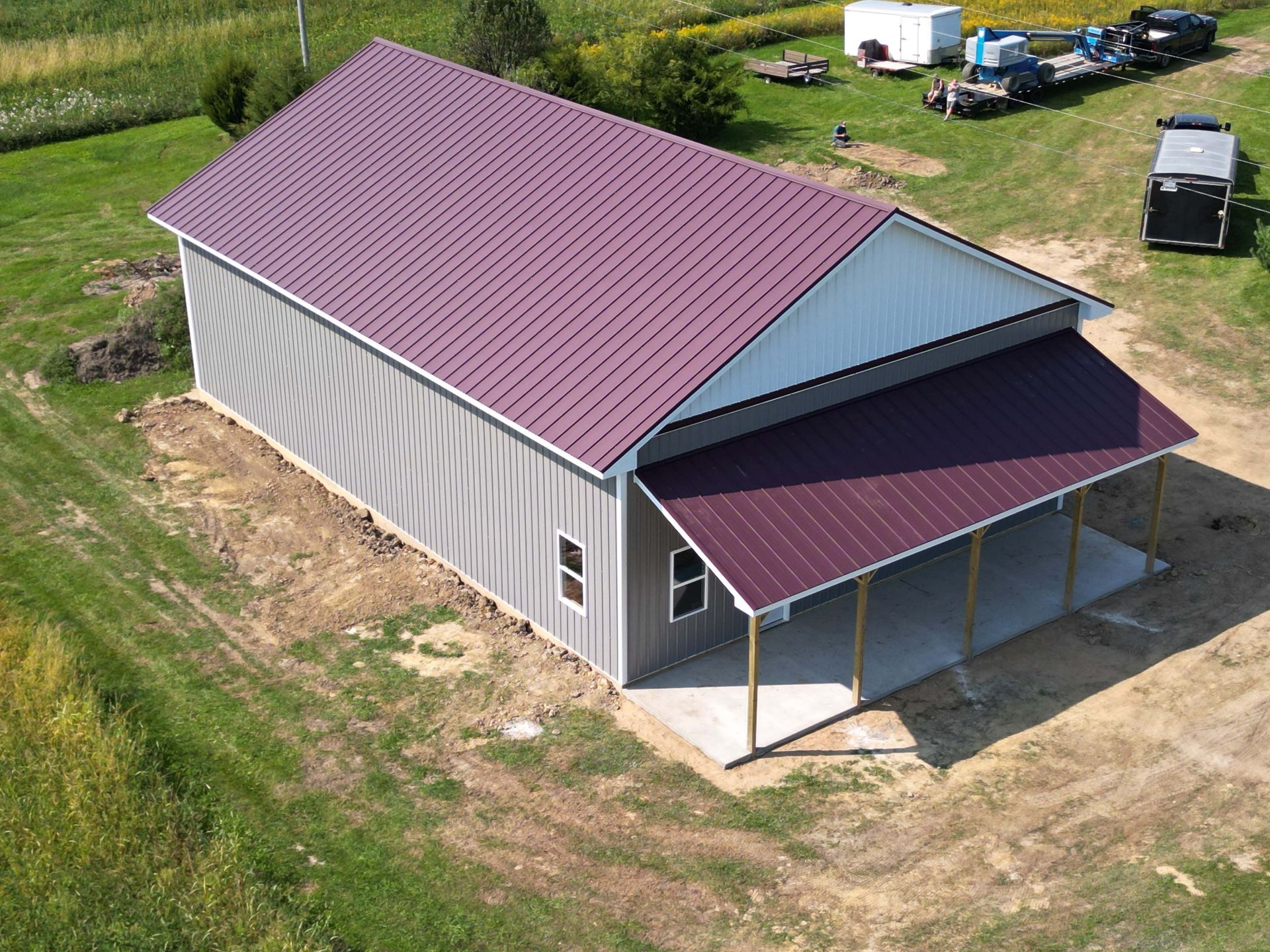 Gray and burgundy metal-roofed barn with a porch, in a grassy field.