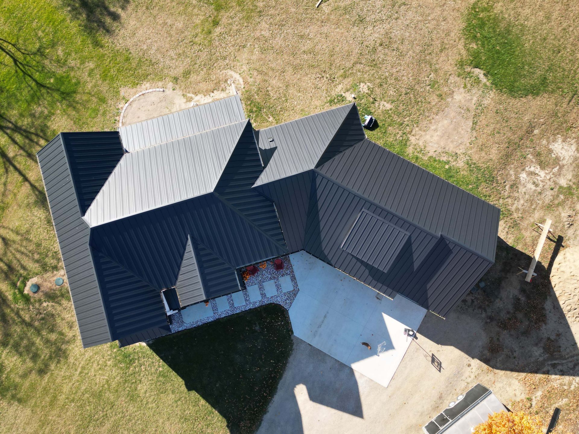 Aerial view of a dark-roofed house with concrete driveway, set on a grassy yard.