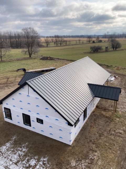 Newly constructed house with silver metal roof, black trim, and wrap, in a field.