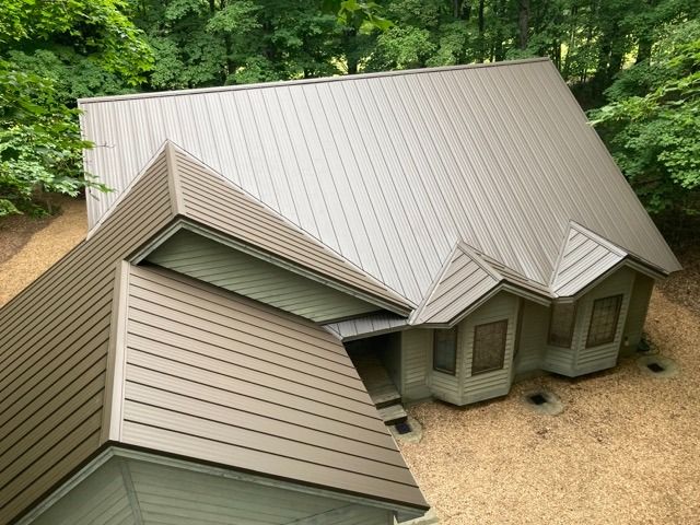 Brown metal roof on a house with windows, surrounded by trees and gravel.