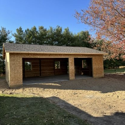 New two-car garage under construction; wooden frame, roof, and concrete floor; outdoors on a sunny day.