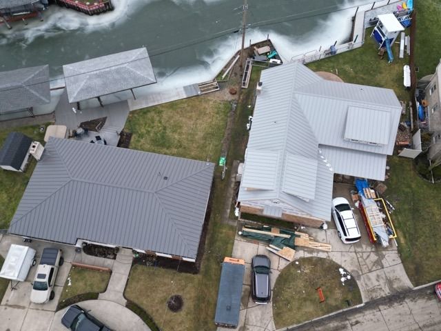 Overhead view of homes near a waterway, with gray roofs, cars in driveways, and a boat dock.