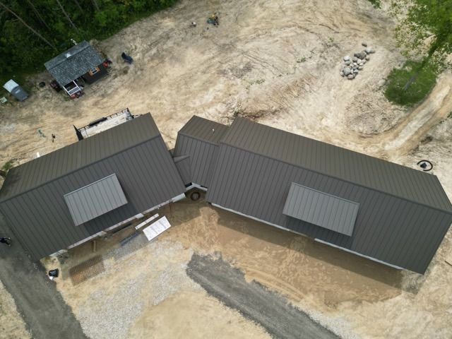 Aerial view of two dark-roofed modular homes side-by-side on a construction site.
