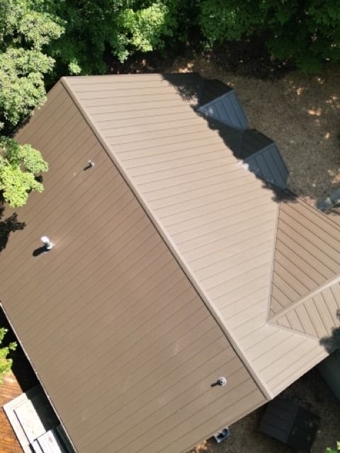 Brown metal roof on a house, viewed from above, surrounded by green trees.