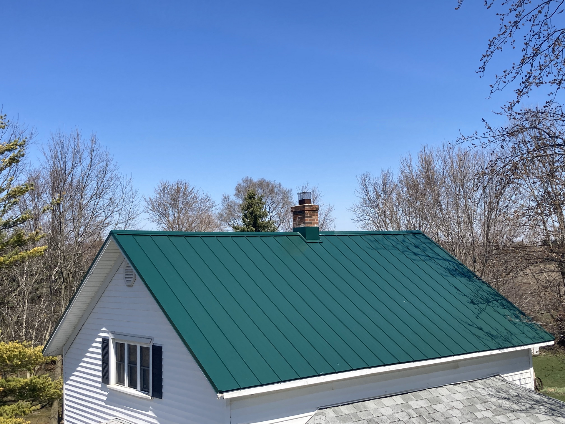 White house with a green metal roof and a chimney against a blue sky.