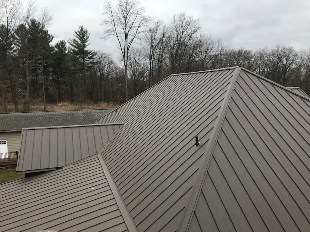 Brown metal roof on a house, with trees in the background under a cloudy sky.