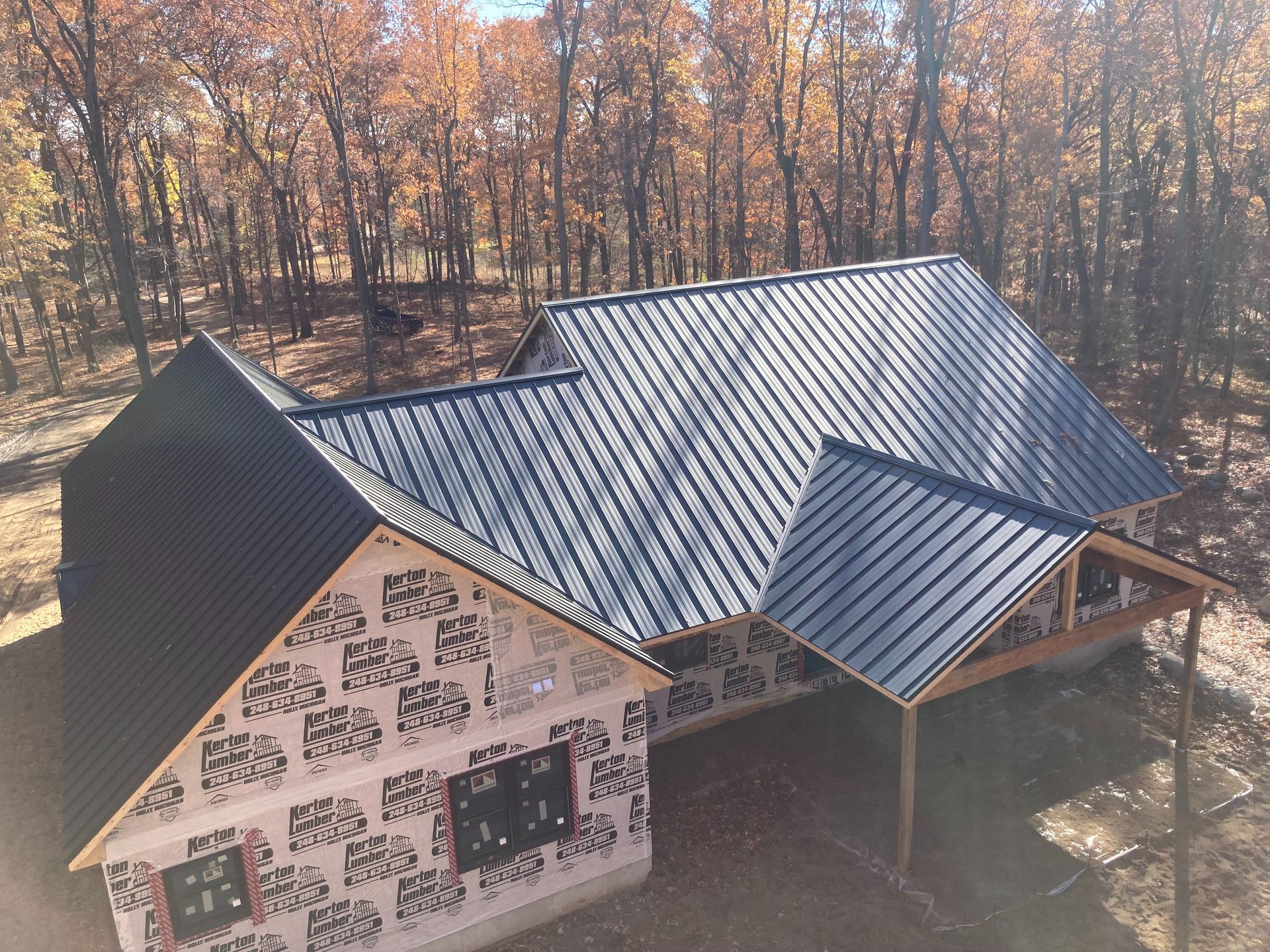 New house under construction with a black metal roof in a wooded area.