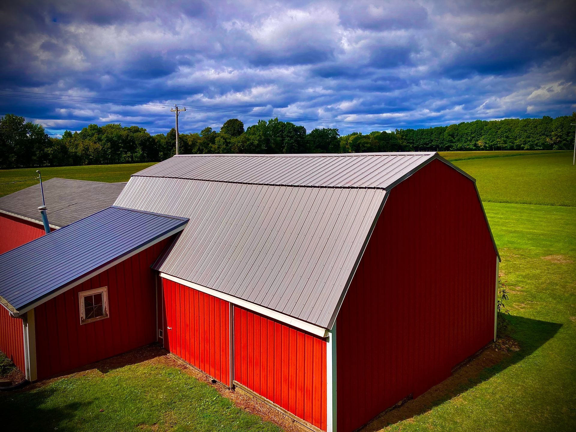 Red barn with gray roof in a green field under a cloudy sky.