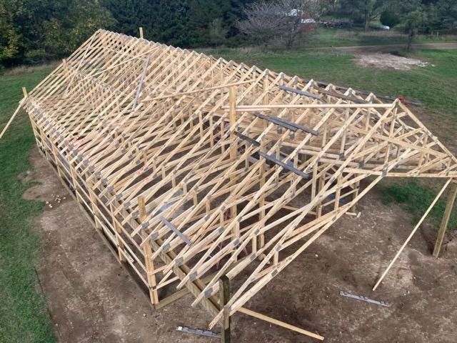 Wooden frame of a building under construction, outdoors on a dirt surface.