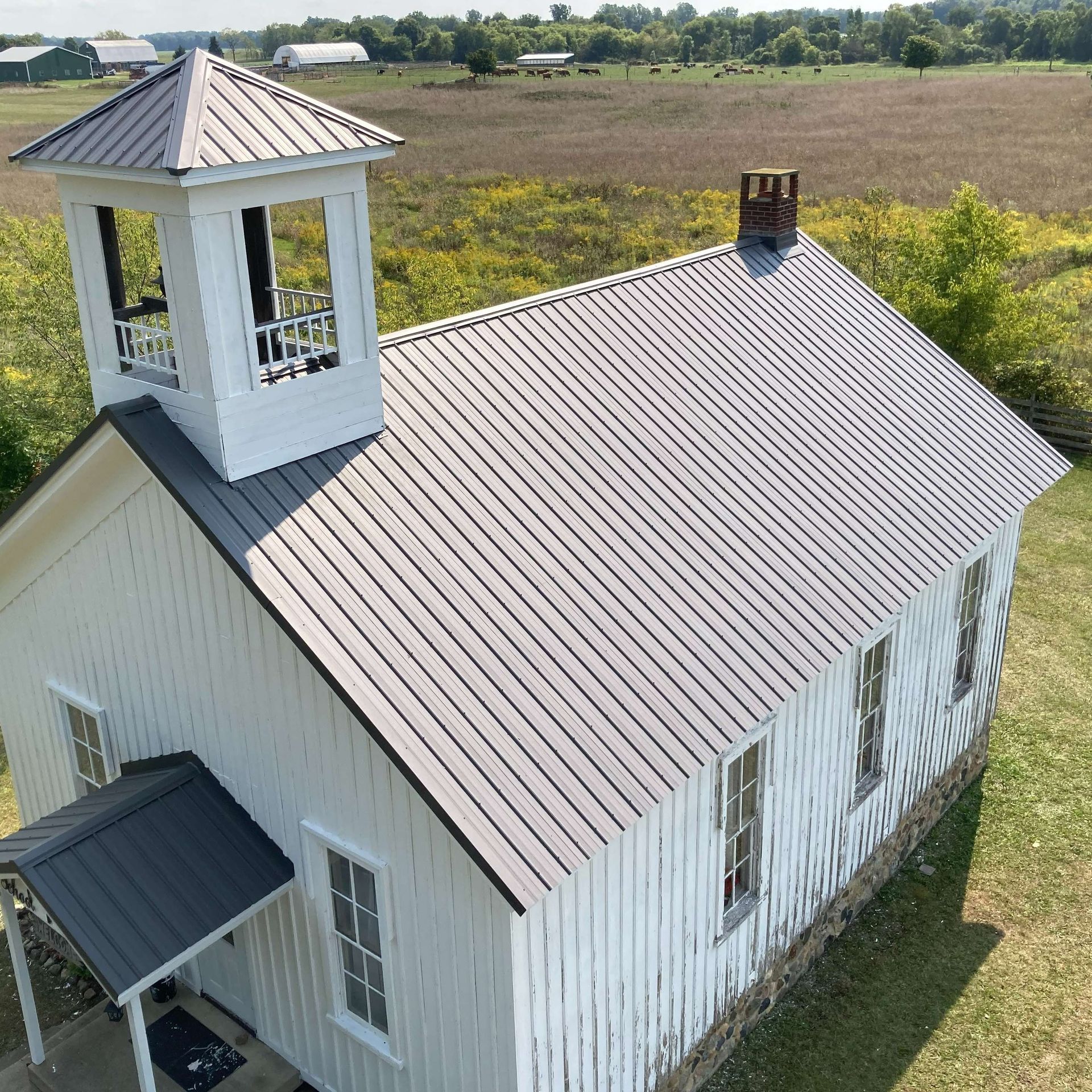 White church with a bell tower and metal roof in a field.
