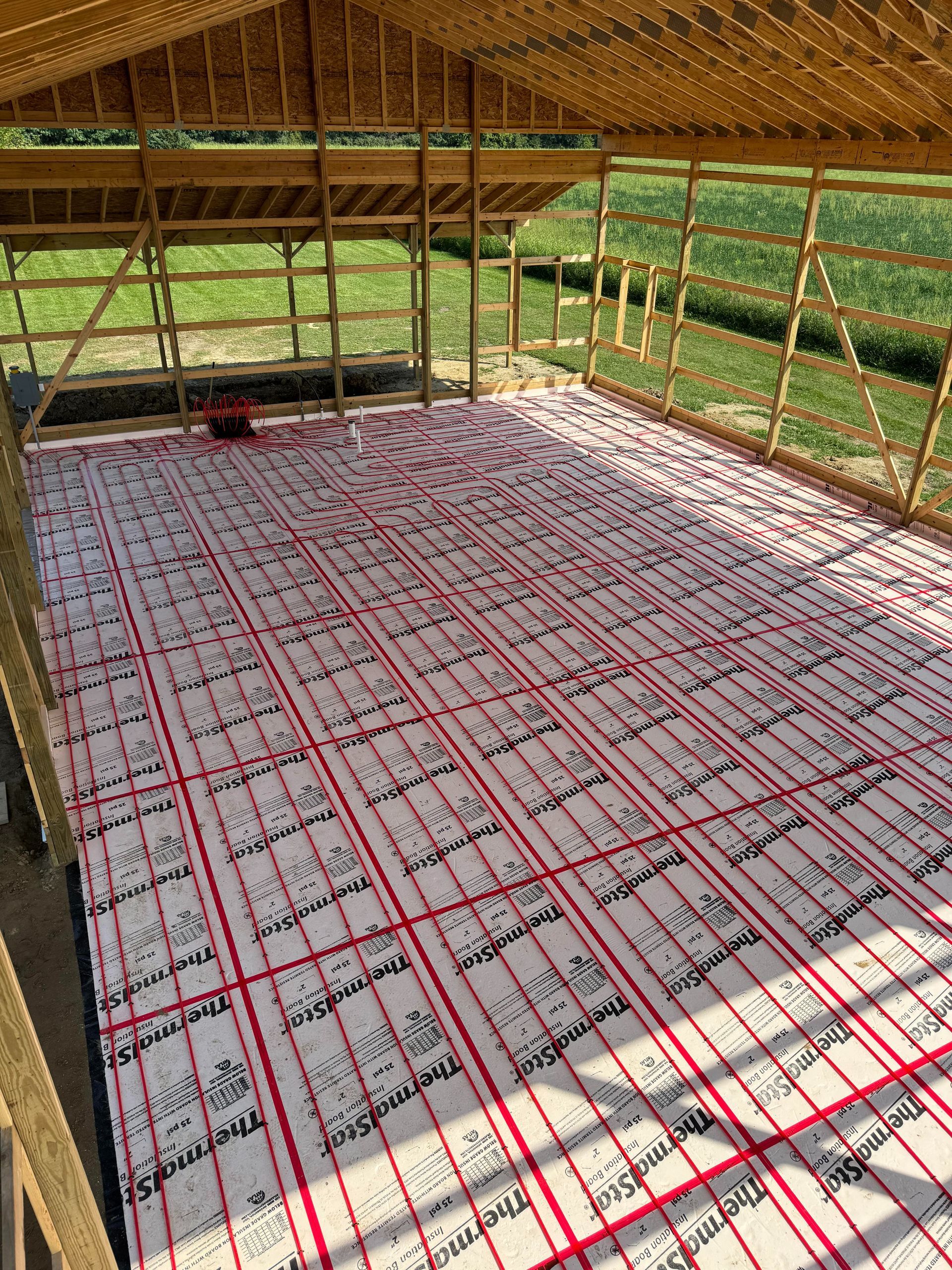 Framing of a building's interior with red radiant floor heating tubes laid over insulation sheets.