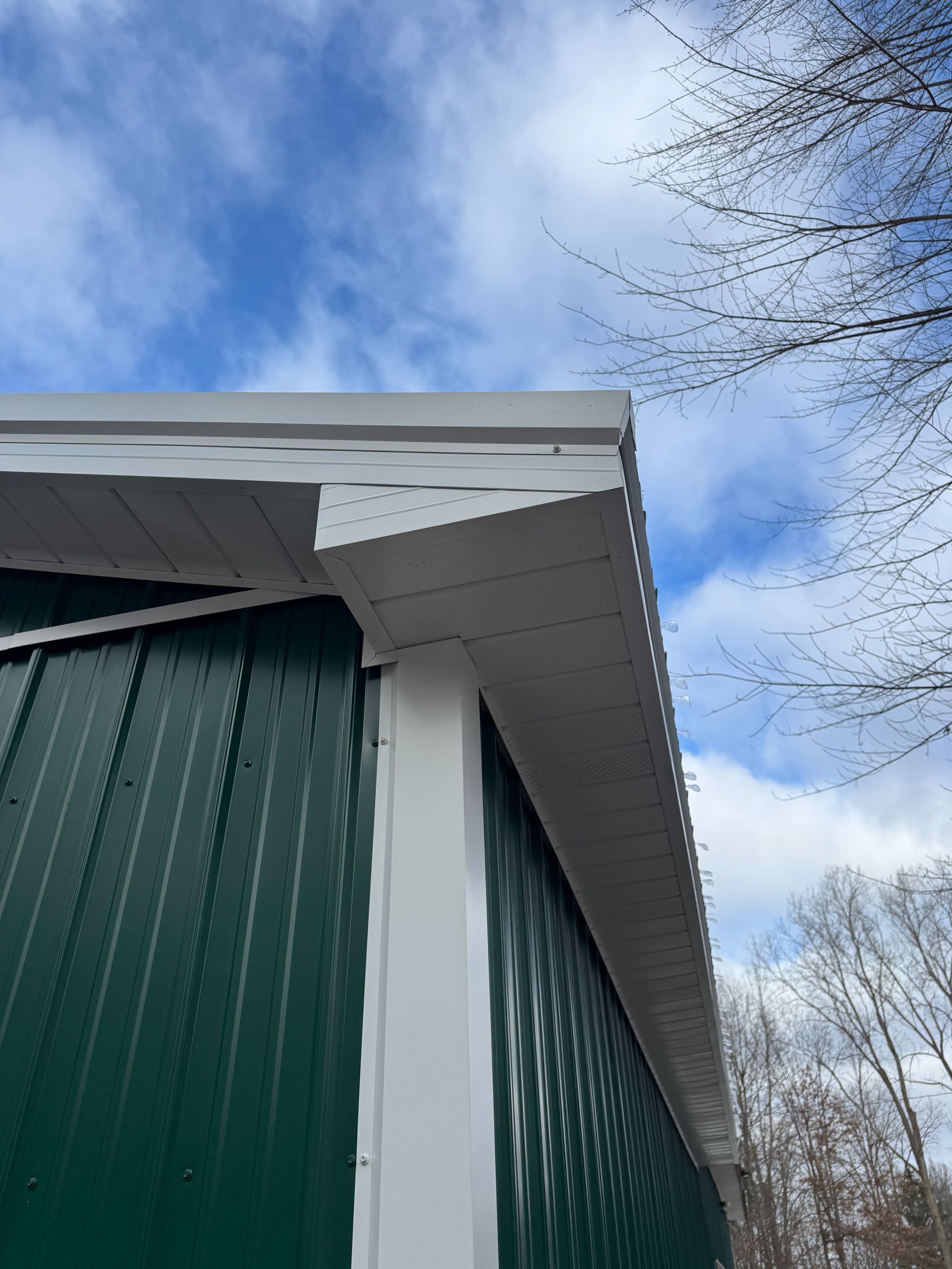 Green metal building with white trim under a cloudy blue sky.