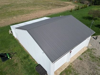 White building with a gray metal roof in a grassy field.