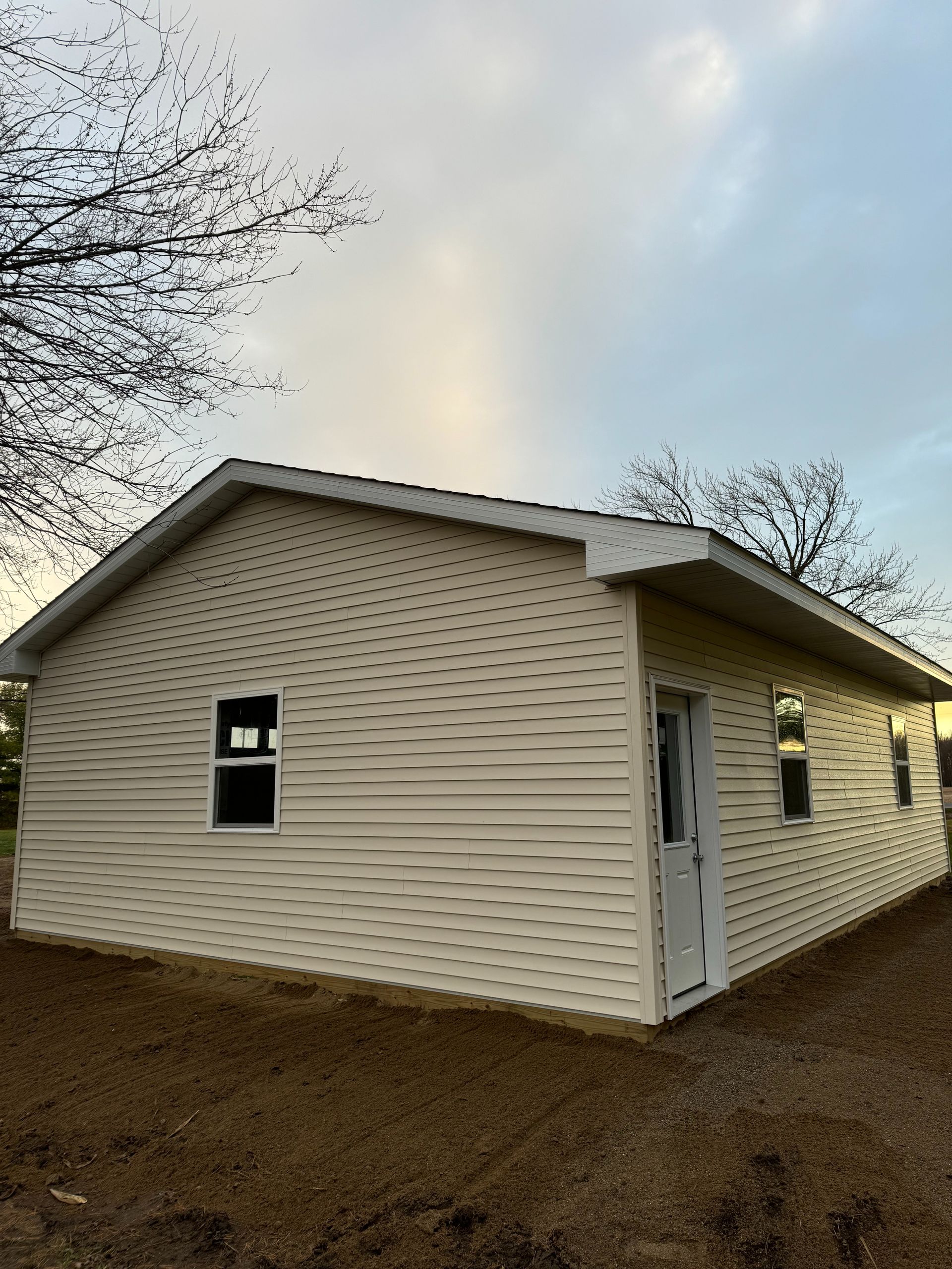 Beige shed with white trim, a small window, and a door, set outside under a cloudy sky.