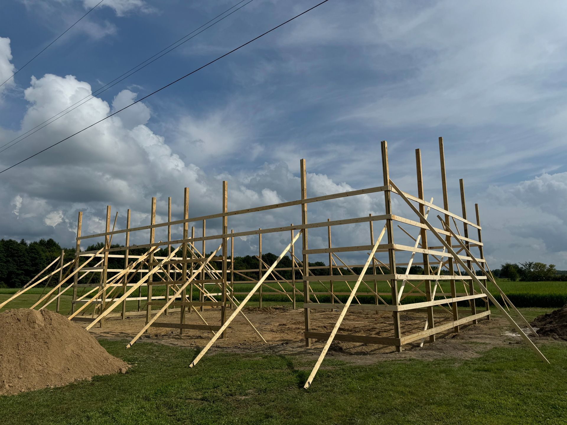 Wooden frame of a barn under construction on a grassy field, under a cloudy sky.