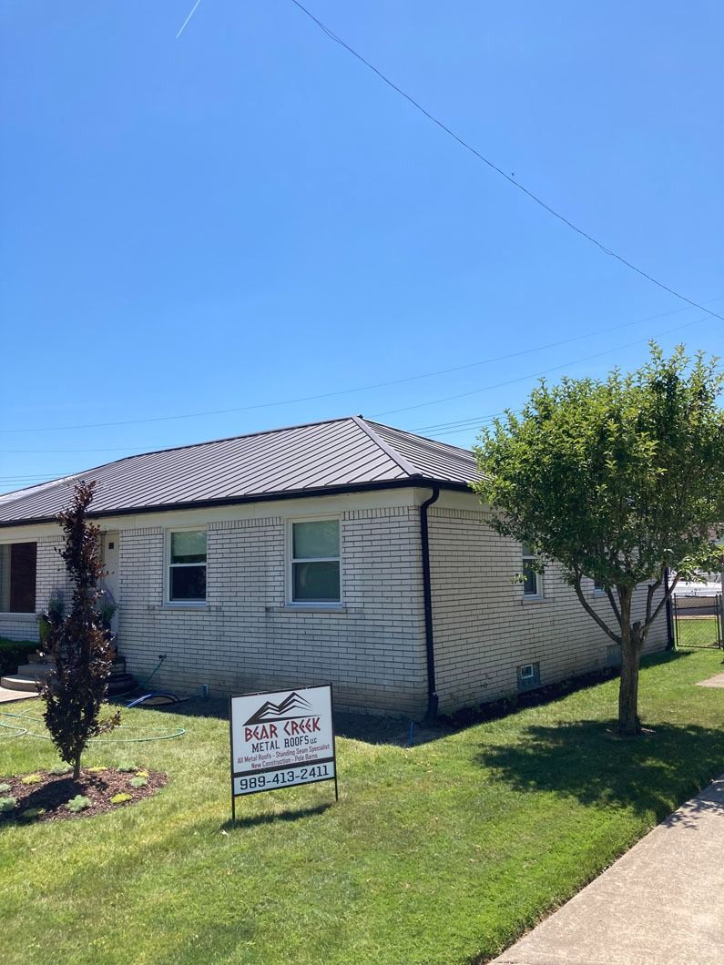 White house with black roof under a blue sky. Real estate sign on the front lawn.