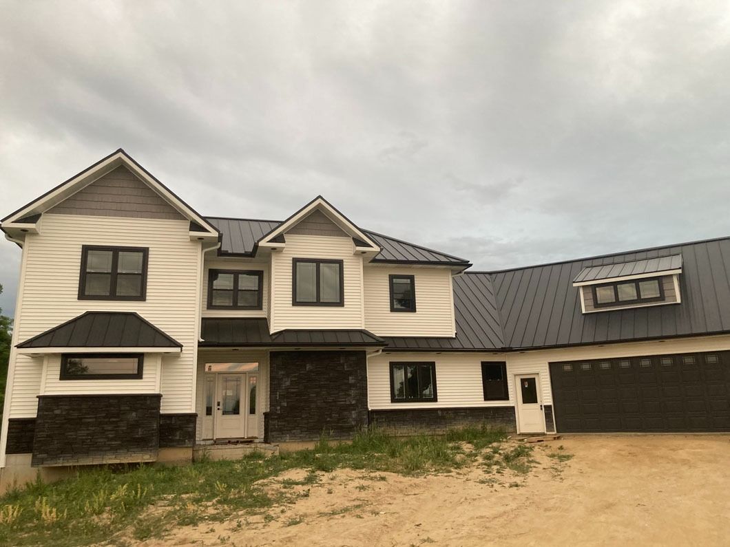 Two-story house under construction with white siding, black roof and dark windows. Gray cloudy sky.