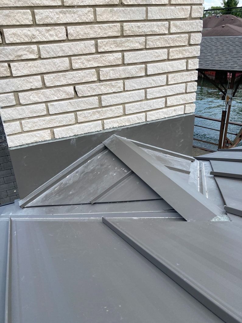 Close-up of a gray metal roof with a brick chimney. Flashing and seams are visible.