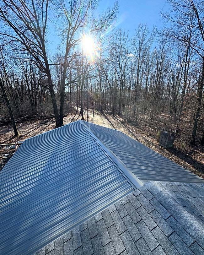 Rooftop with new shingles, sun shining through trees in the background.