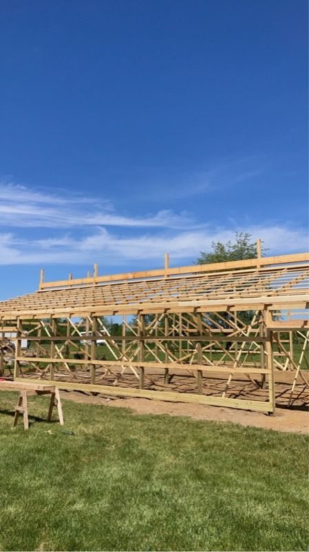 Wooden frame of a building under construction on a grassy field, against a blue sky.