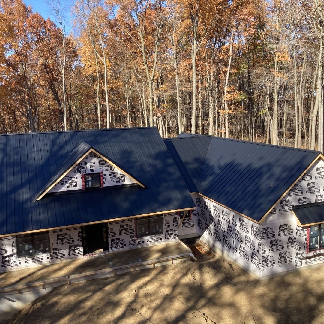 House under construction with dark blue roof, surrounded by trees with fall foliage.