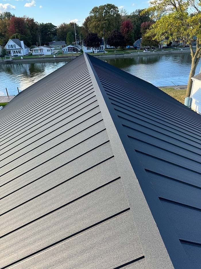 Dark gray metal roof overlooking a body of water with houses and trees in the background.