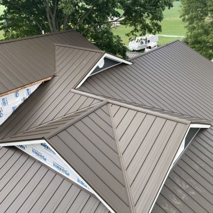 A brown metal roof with angled lines and triangular sections, against a backdrop of trees and a vehicle.