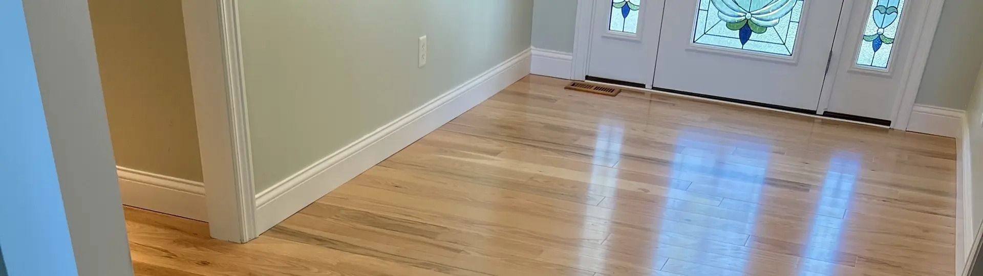Hardwood floor in an entryway with white trim and a white door with windows.