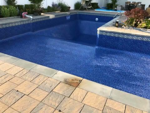 A large blue swimming pool is surrounded by a brick patio.