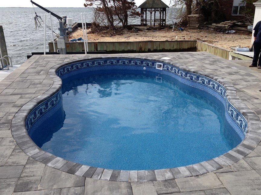 A large swimming pool surrounded by bricks next to a body of water.