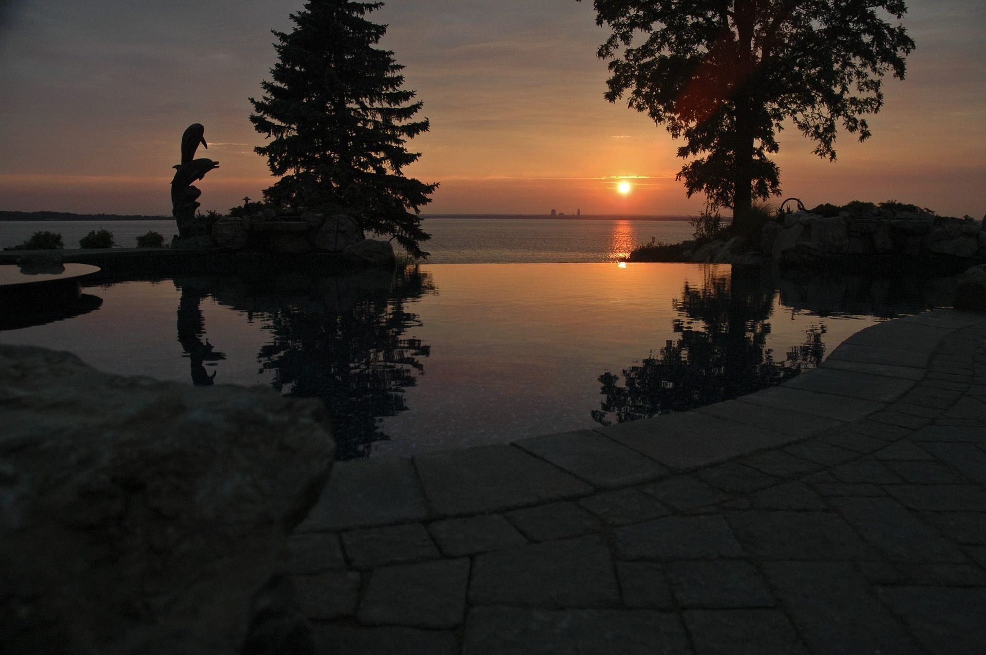 A sunset over a large body of water with trees in the foreground