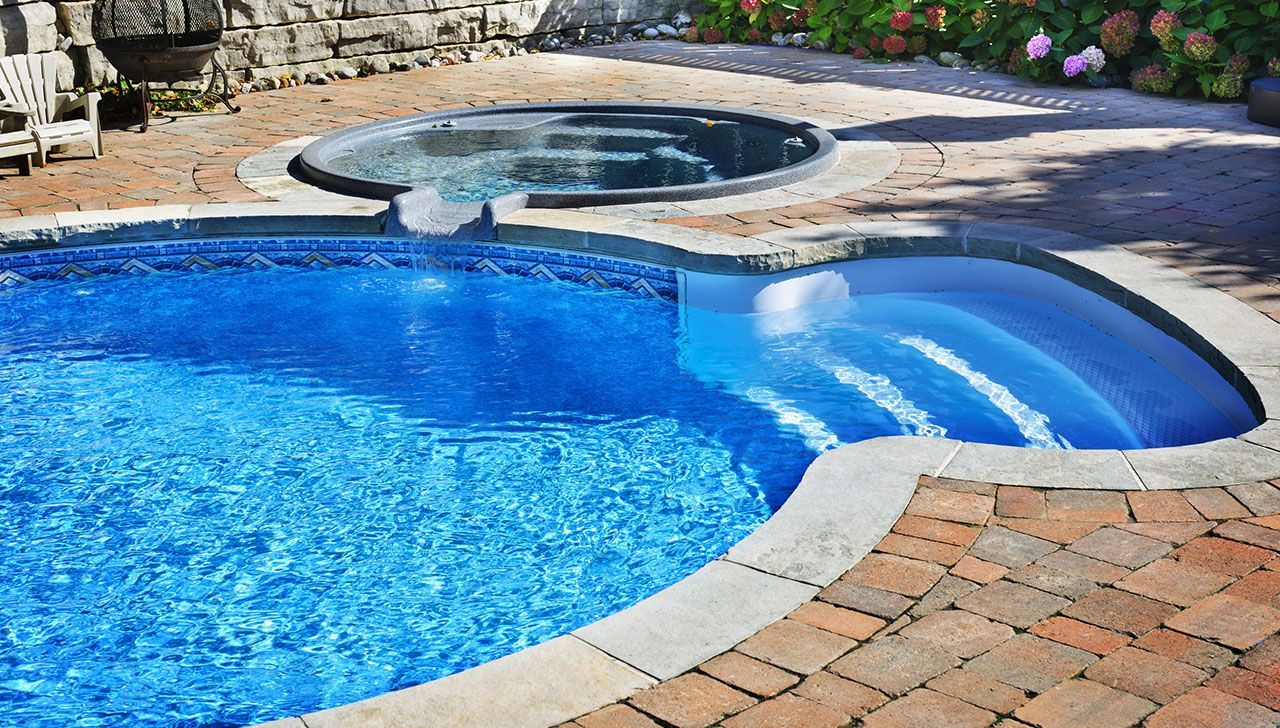 A large swimming pool with stairs and a hot tub in the backyard.